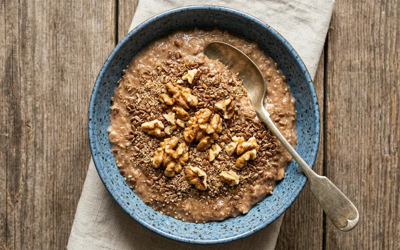 A blue bowl of porridge topped with walnuts and ground flaxseed